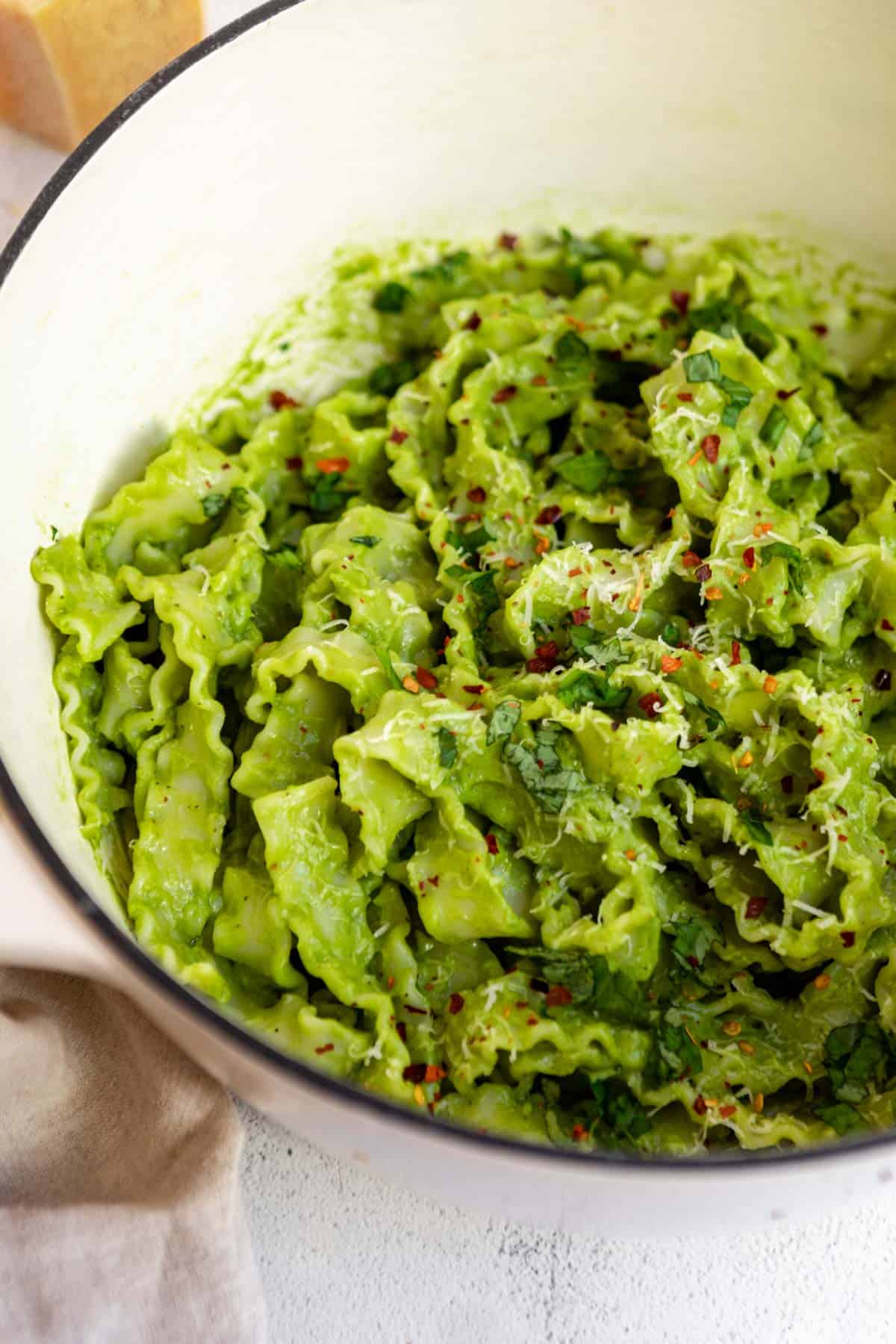 Long strands of spaghetti being tossed with a generous amount of green avocado pesto in a cooking pot.