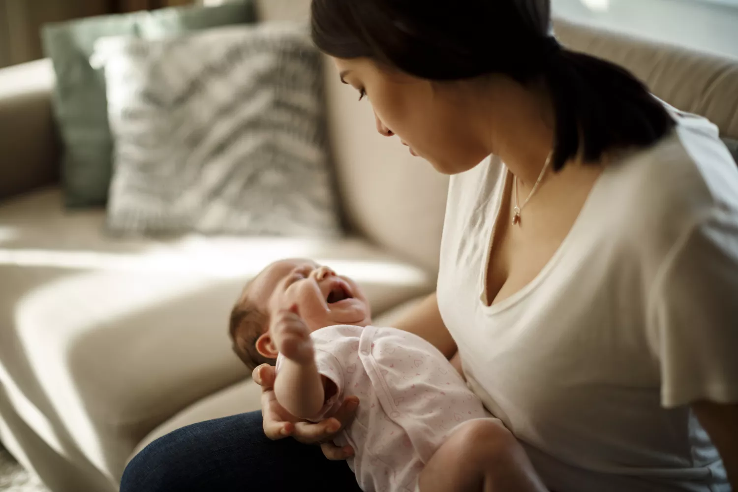 A stressed caregiver sitting on a sofa while holding a crying newborn baby.