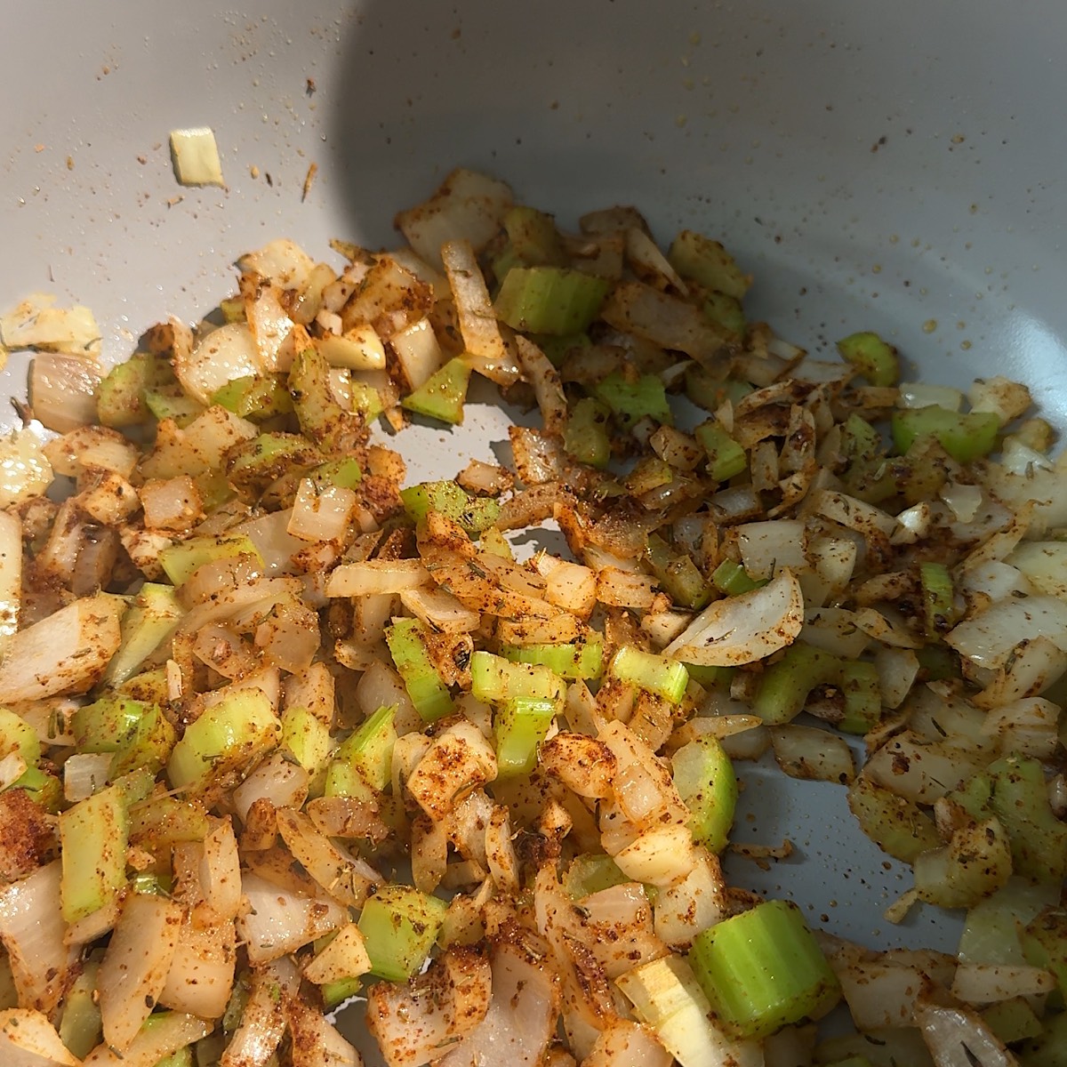 Diced vegetables and spices being sautéed in a large metal pot.