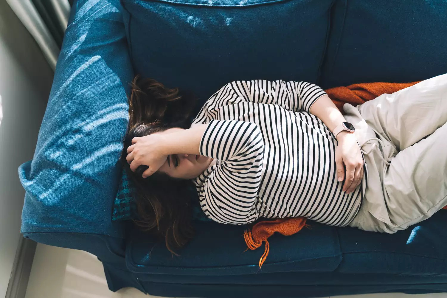 A person lying on a couch in visible distress, holding their flank area where kidney pain typically originates.