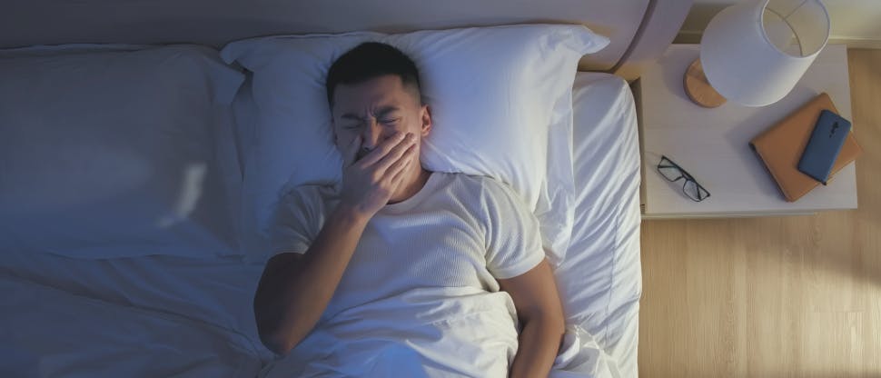 A person sitting up in bed at night looking distressed and unable to sleep due to pain.
