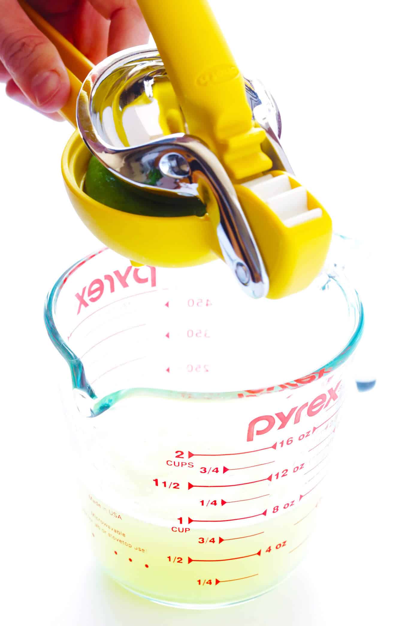 Fresh lime juice being measured into a glass cup alongside fresh citrus fruits.