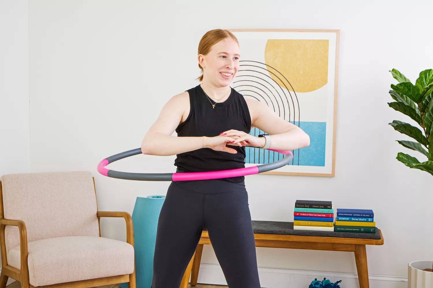 A woman smiling while using a pink and gray weighted hula hoop for core exercise.