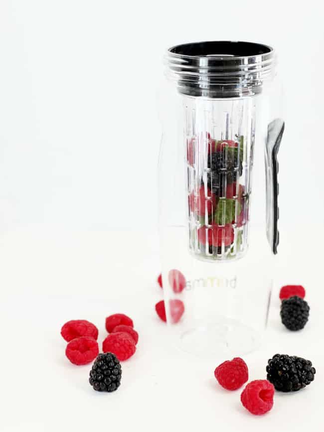 A clear glass filled with water and floating slices of fresh citrus and berries.