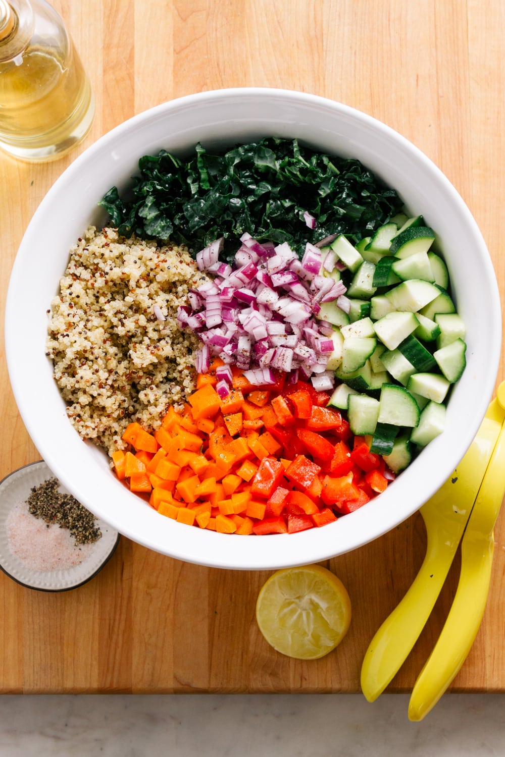 Chopped vegetables and cooked quinoa being added to a large white mixing bowl on a wooden surface.