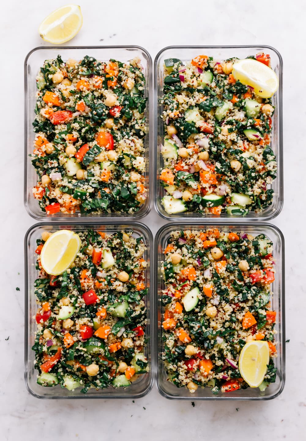 Four glass meal prep containers filled with portions of the kale and quinoa salad.