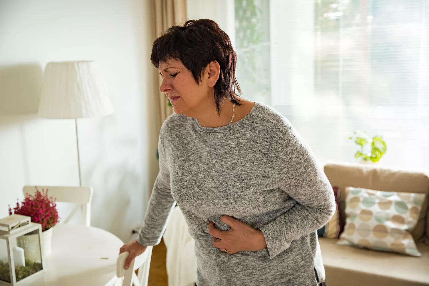 A person sitting on a sofa holding their abdomen with an expression of discomfort.