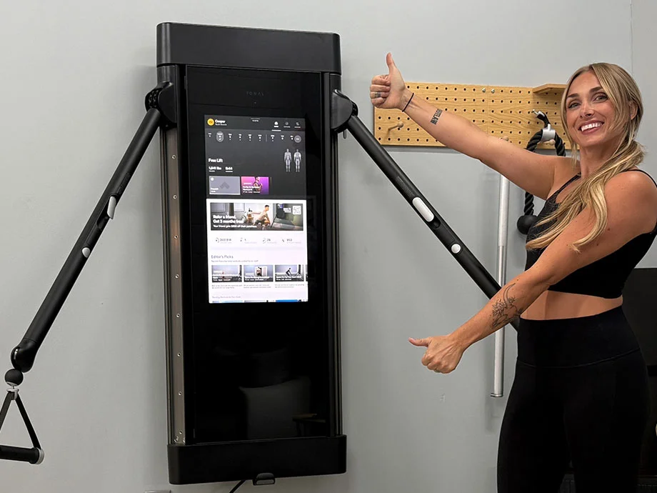 A woman using the wall-mounted Tonal smart gym system.