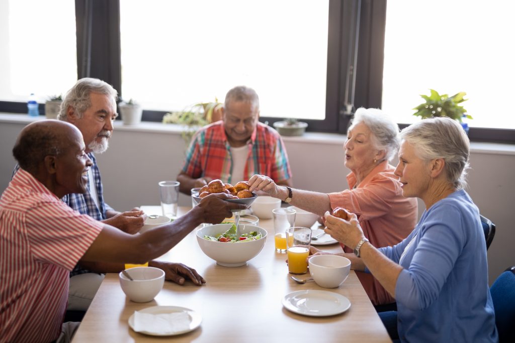 A male caregiver sitting and talking with an elderly man during lunch.