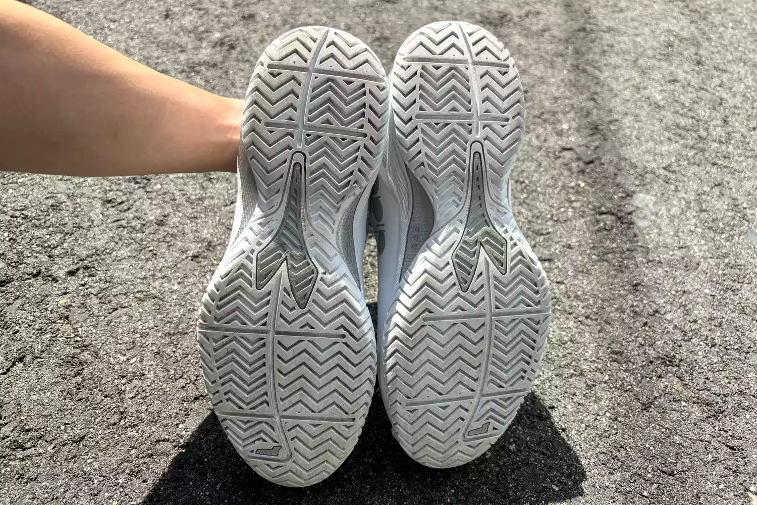 A person holding up a tennis shoe to show the zigzag tread pattern on the sole.