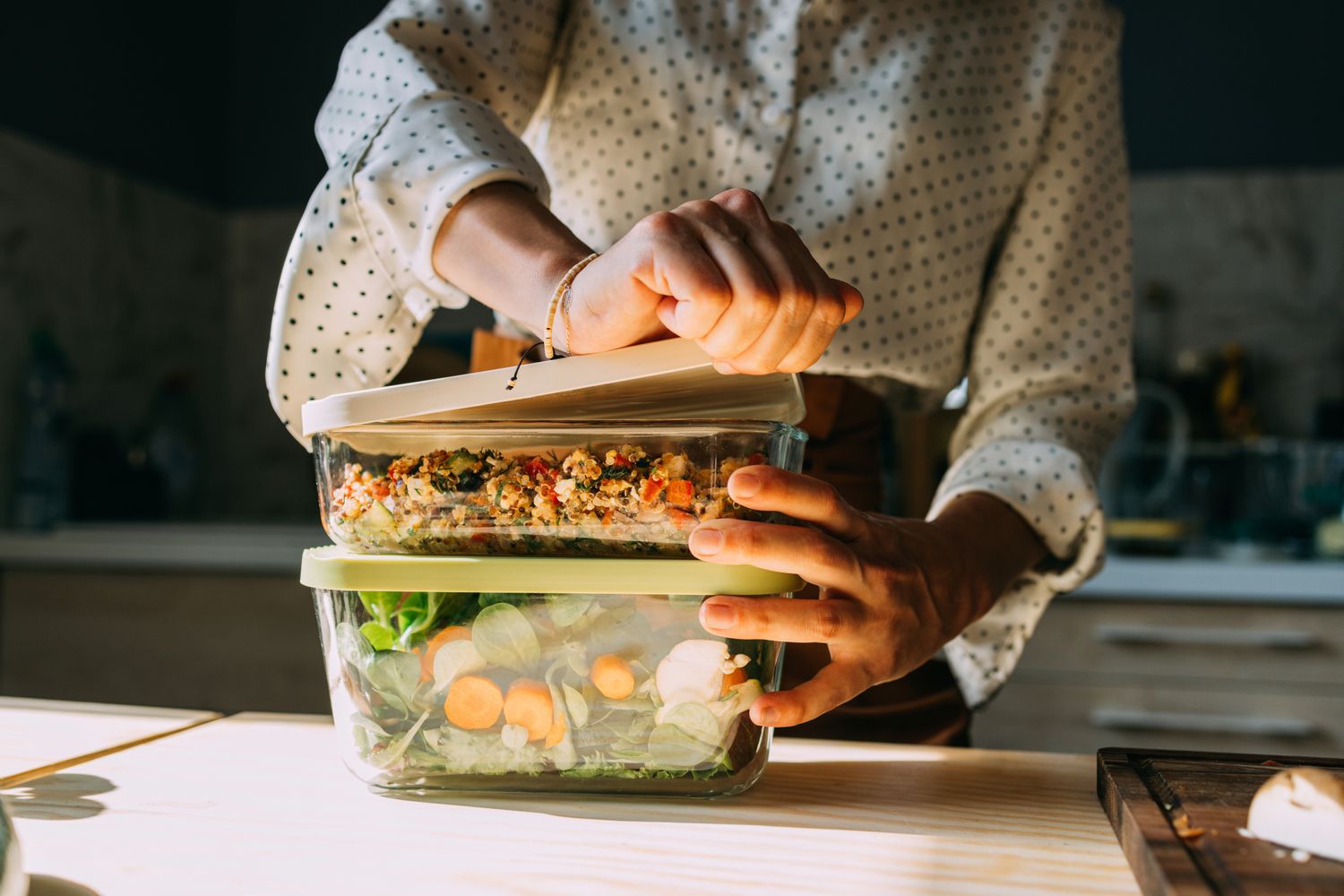 A person organizing pre-prepared meal containers filled with fresh vegetables and grains.