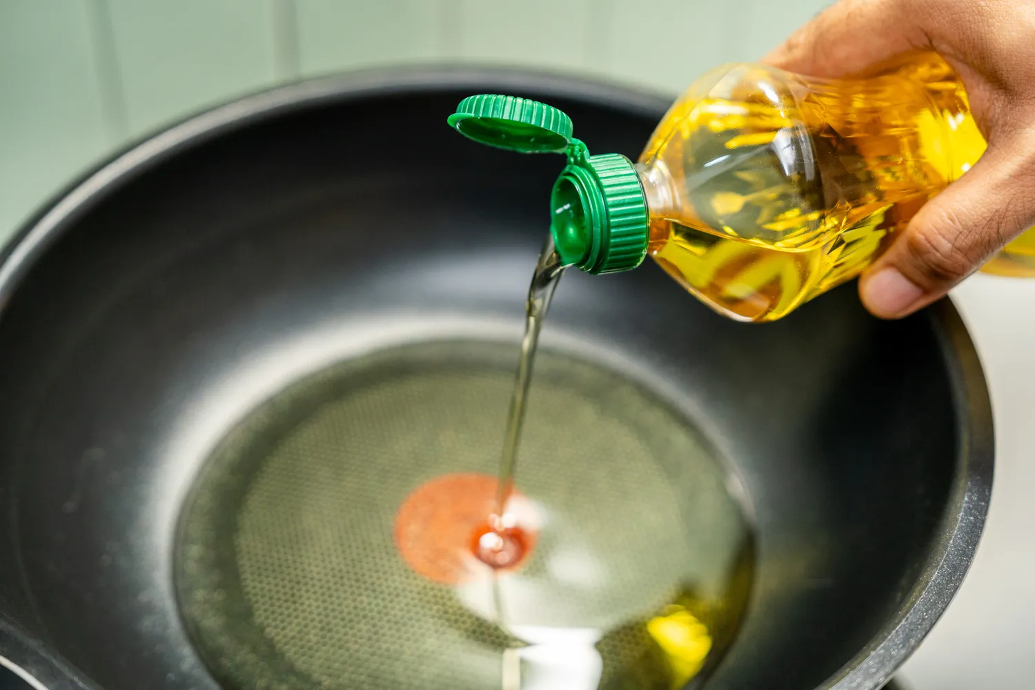 A close-up of a hand pouring clear vegetable oil into a pan.