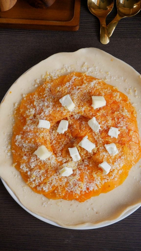 Hands carefully folding the edges of a shaggy pastry dough over a circular arrangement of sliced fruit.
