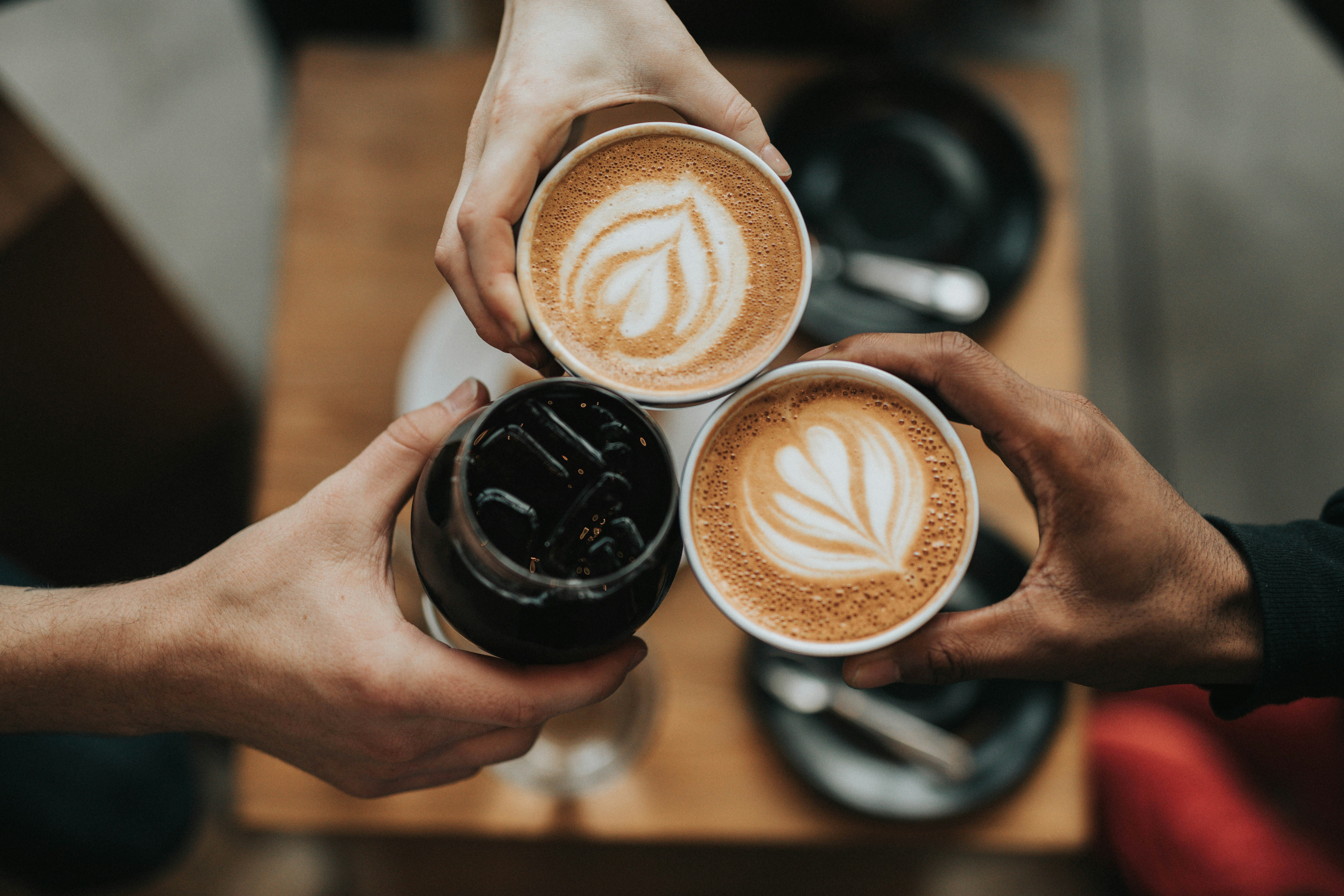 A cup of coffee sitting on a desk next to a person working on a laptop.