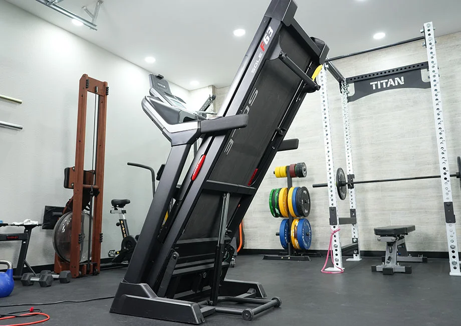 A Sole F63 treadmill folded vertically in a home gym corner to save floor space.