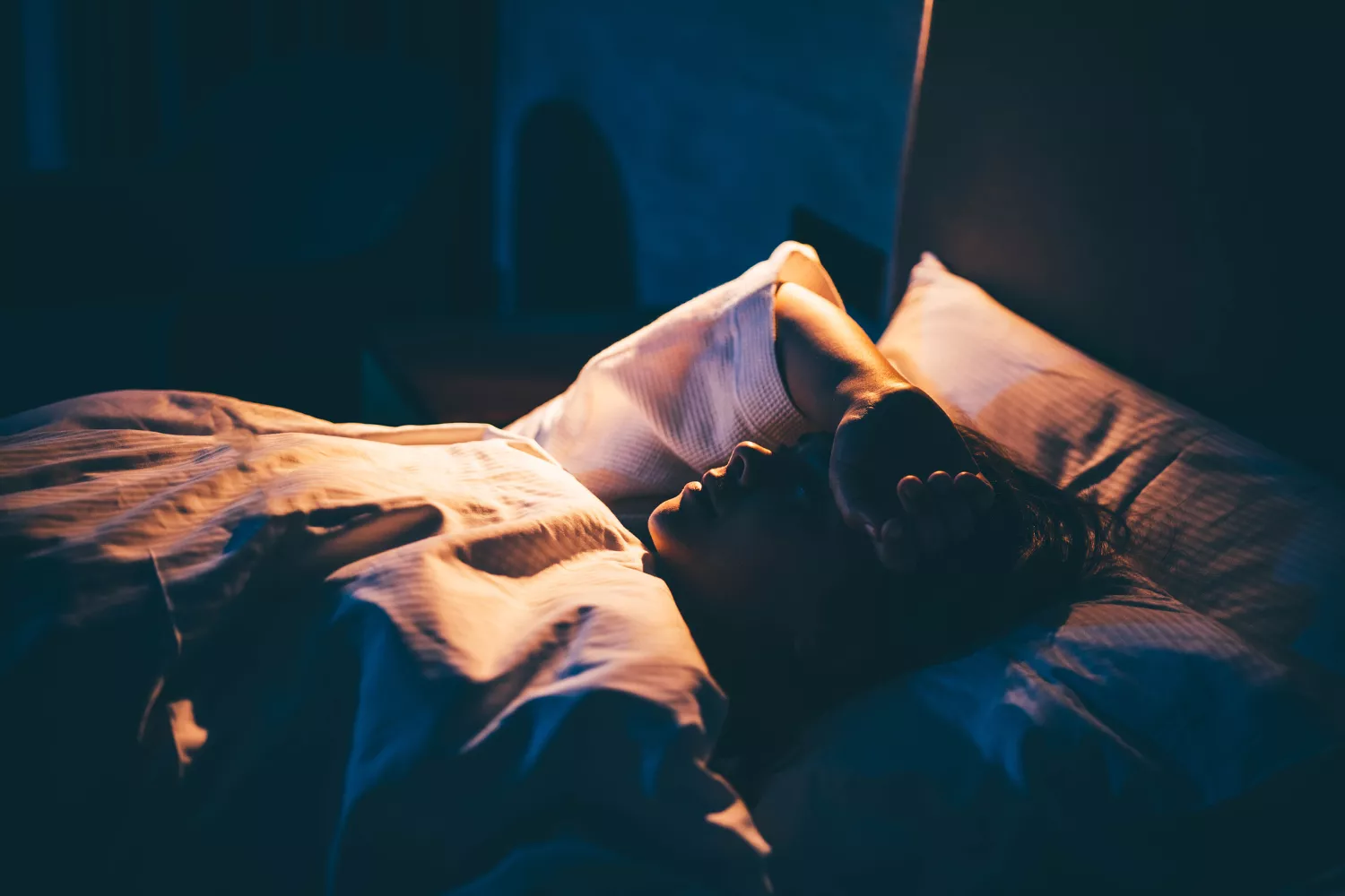 A woman lying in bed looking stressed and unable to sleep in a dark room.