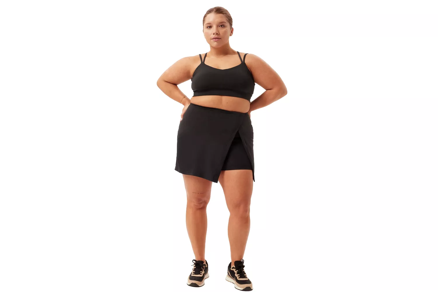 A woman in a black athletic skort and sports bra posing confidently.
