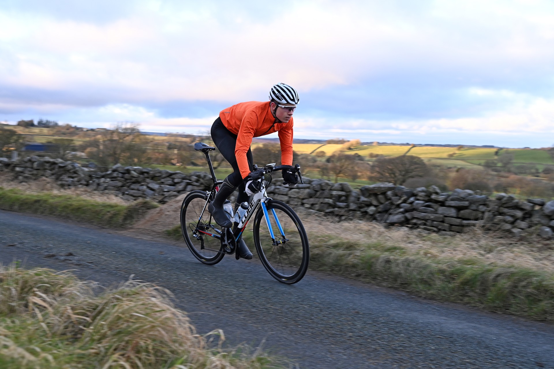A cyclist in cycling kit riding out of the saddle on a hill during a training session.