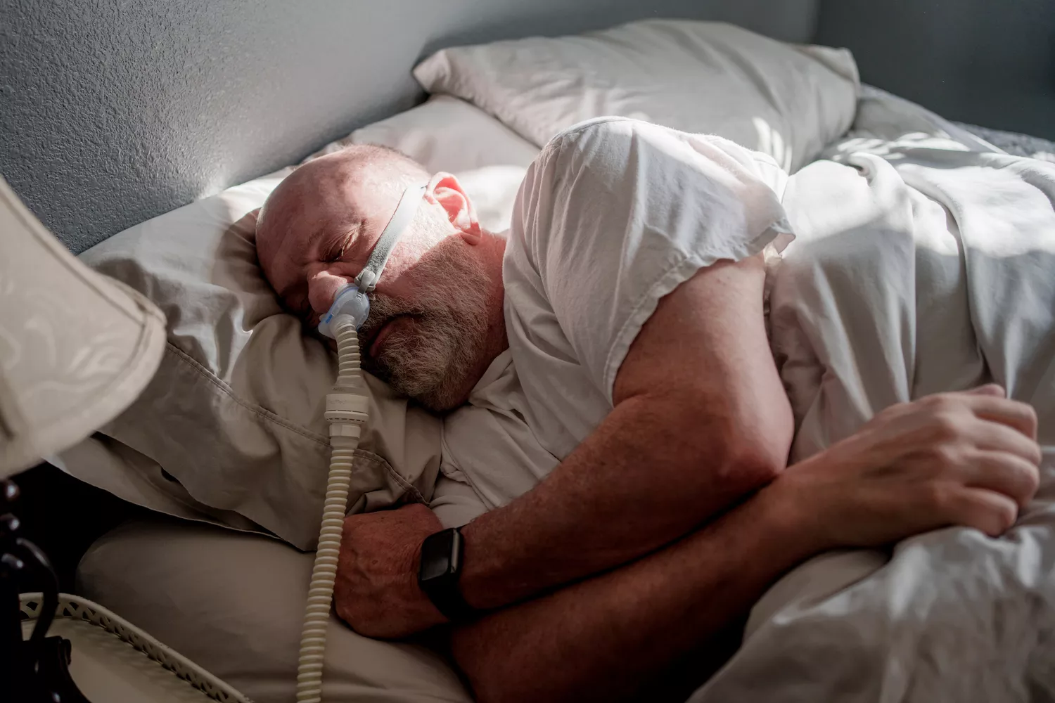 A person in bed wearing a CPAP mask and headgear used for treating sleep apnea.