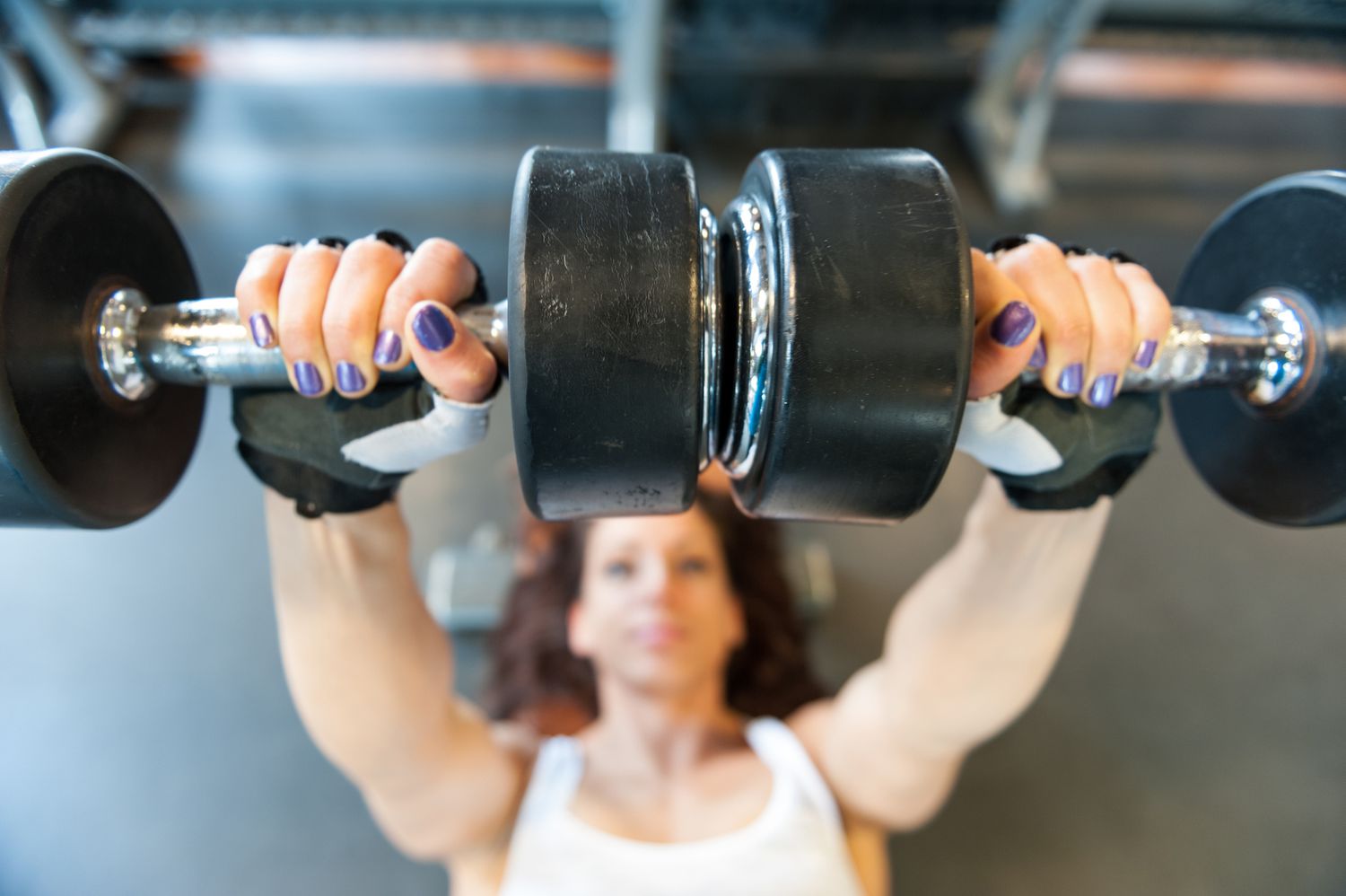 A woman in a gym performing an overhead dumbbell press.