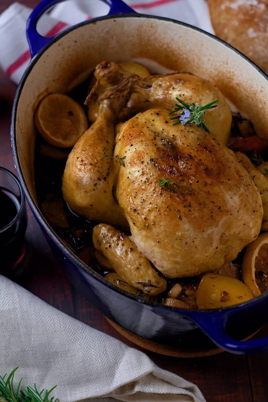 A finished roast chicken and vegetables inside an enamelled Dutch oven, ready for serving.