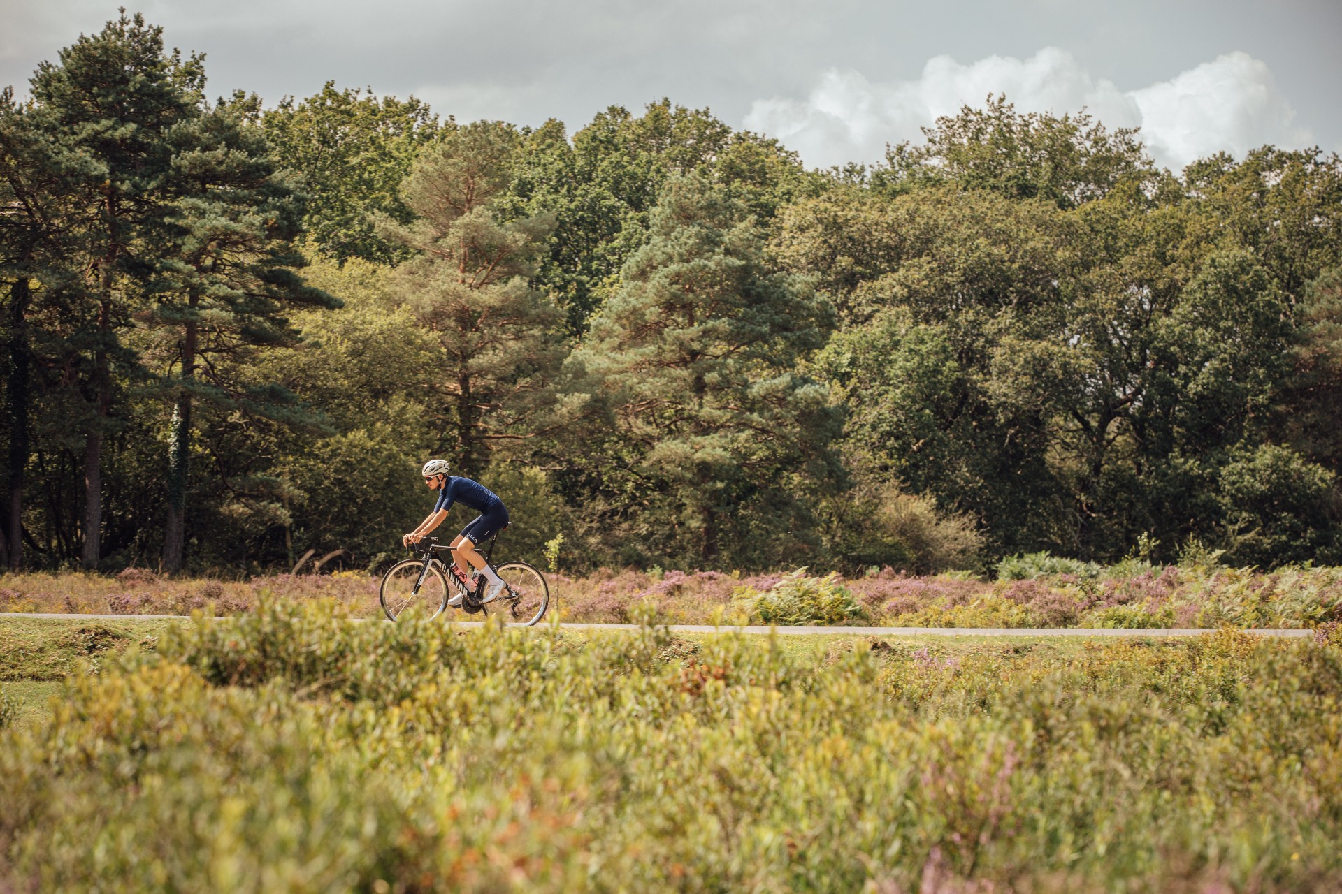 A cyclist riding at a steady pace on an open country road under a clear sky.