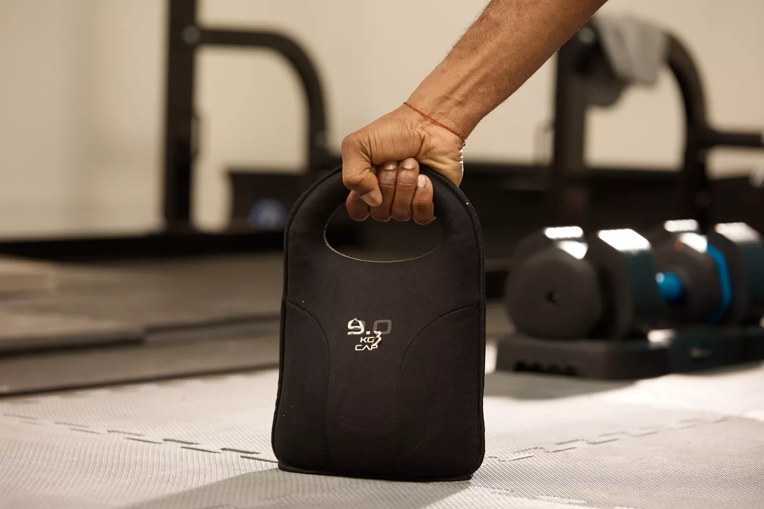 A person's hand gripping a black CAP soft kettlebell on a gym mat.