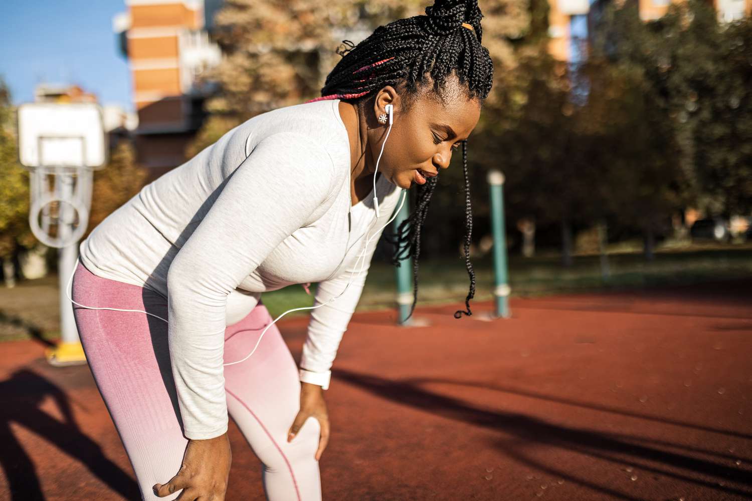A woman in athletic gear leaning over with hands on knees to catch her breath on a track.