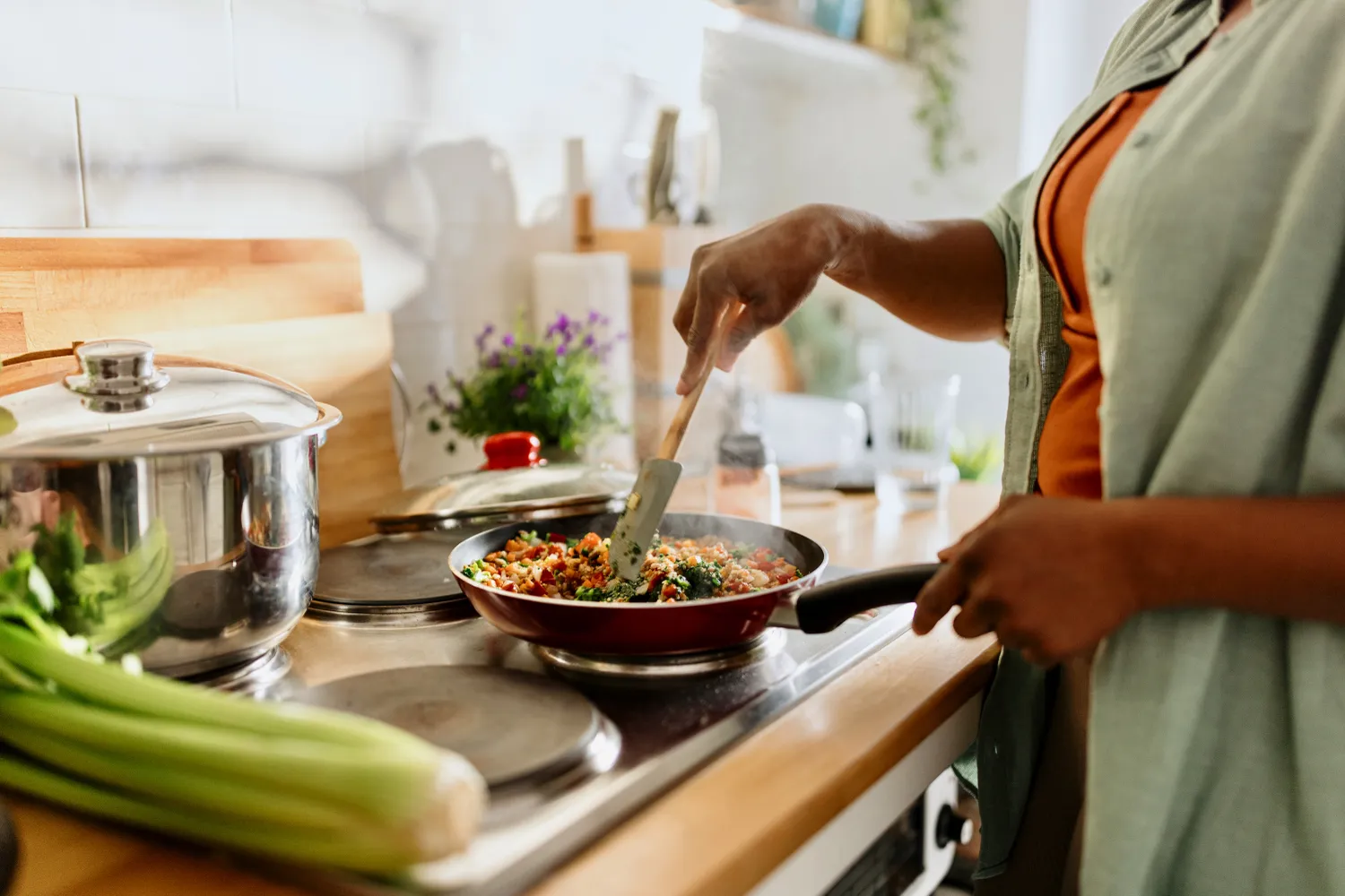 A person cooking a healthy quinoa and vegetable stir-fry in a skillet.