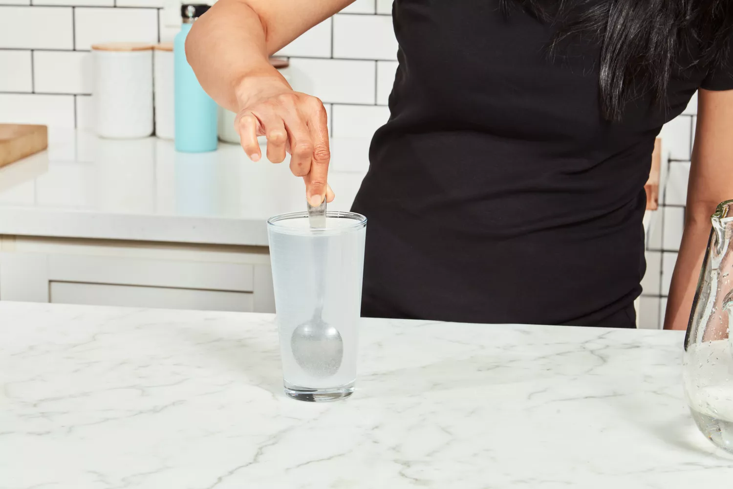 A person stirring a powdered supplement mix into a glass of water on a modern kitchen countertop.