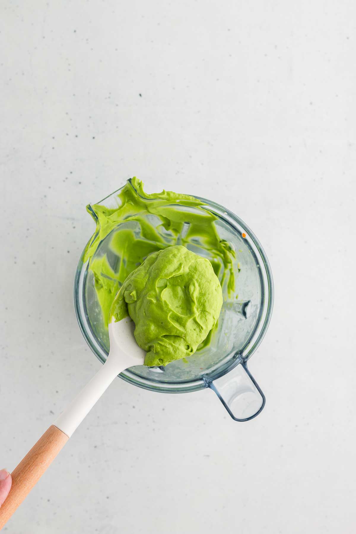 A spoon scooping up thick, smooth green avocado sauce to show its creamy texture.