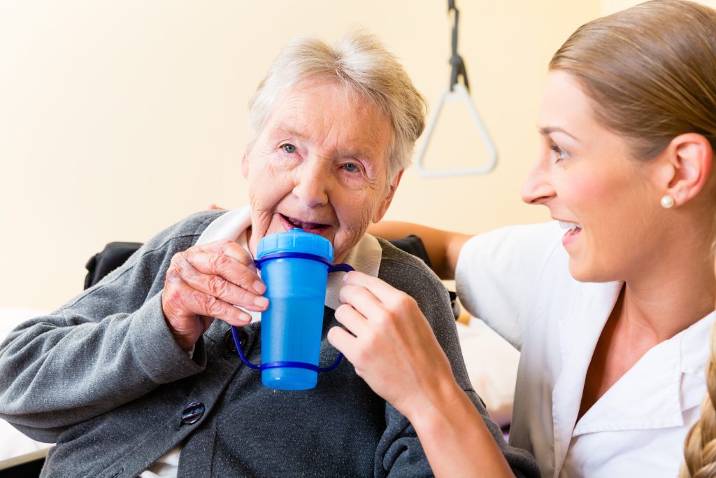 An elderly person holding a glass of water while sitting at a dining table.