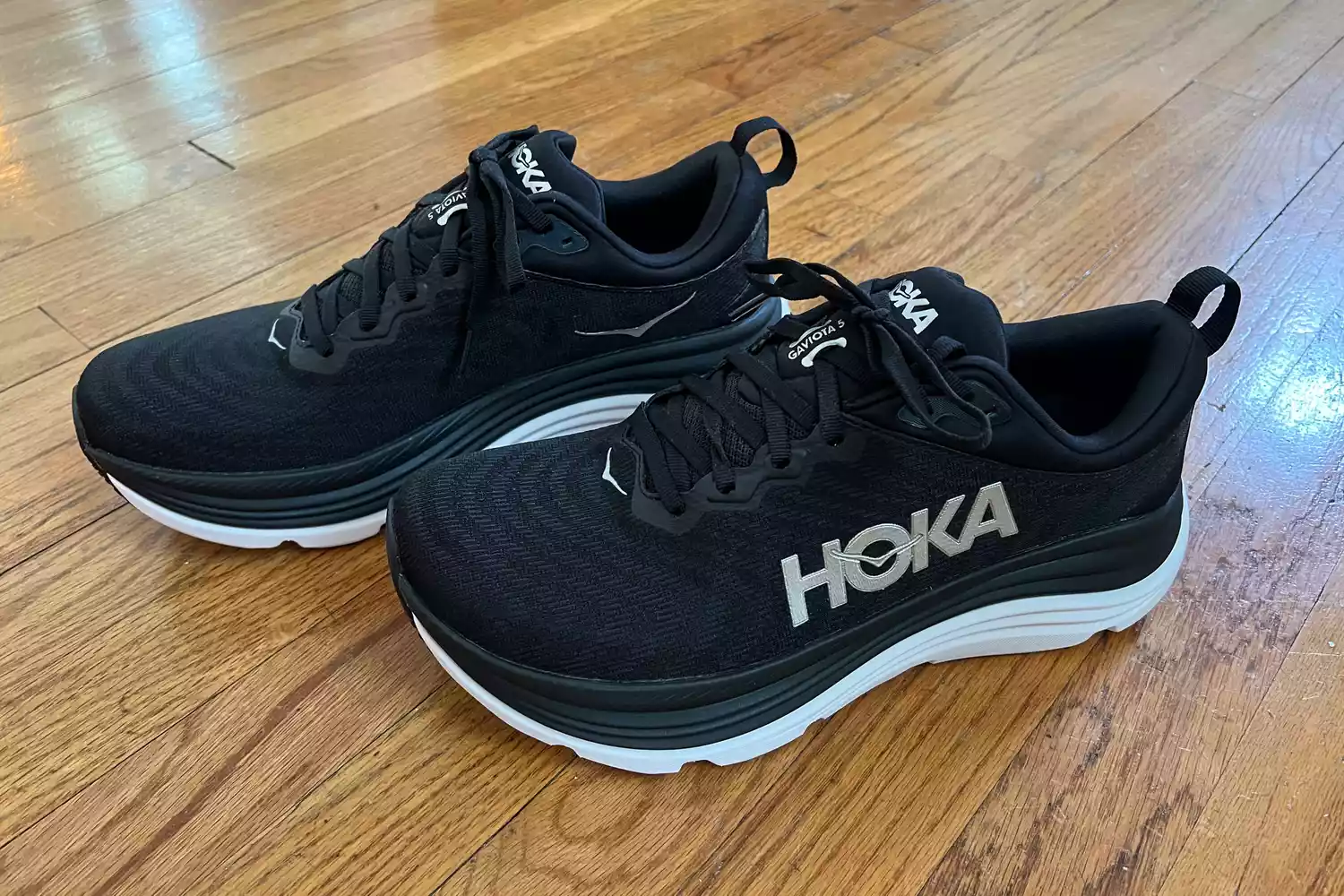 Side profile of black Hoka Gaviota 5 running shoes on a wooden surface.