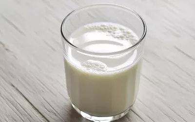 A clear glass filled with white milk resting on a light-colored wooden table.