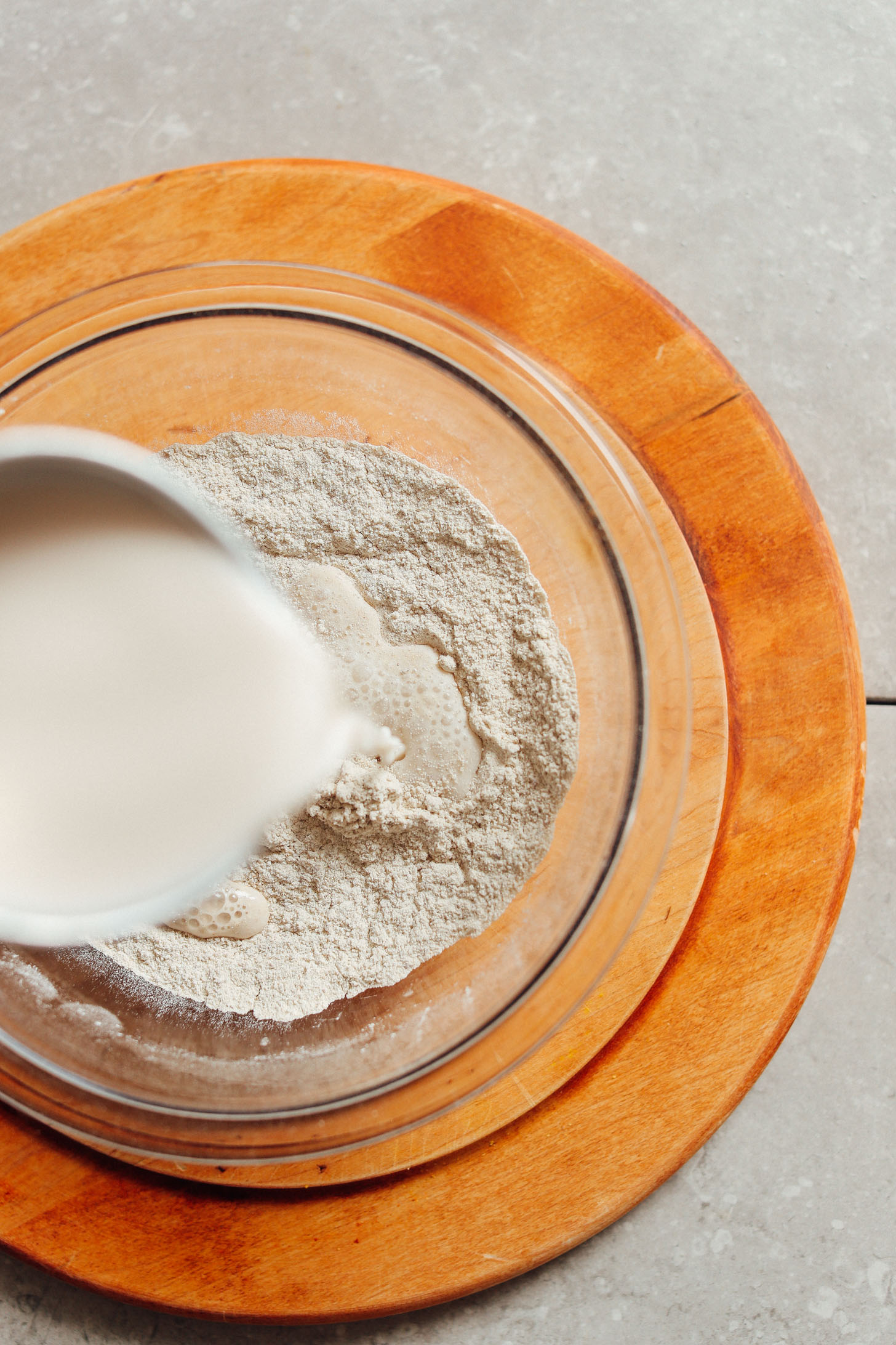 A hand mixing wet and dry ingredients in a glass bowl to create a smooth buckwheat crepe batter.