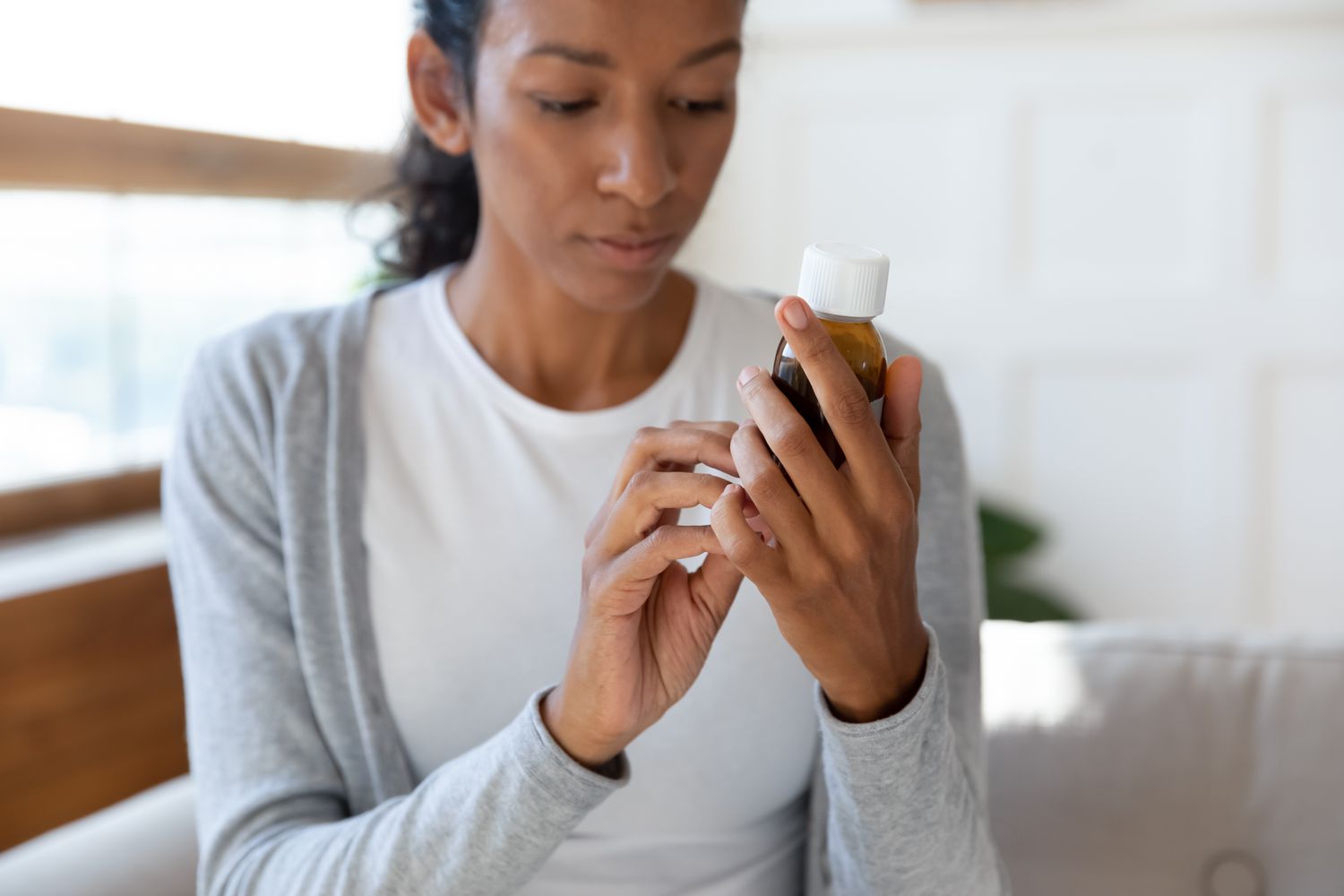 A person holding a brown medication bottle and reading the prescription label carefully.