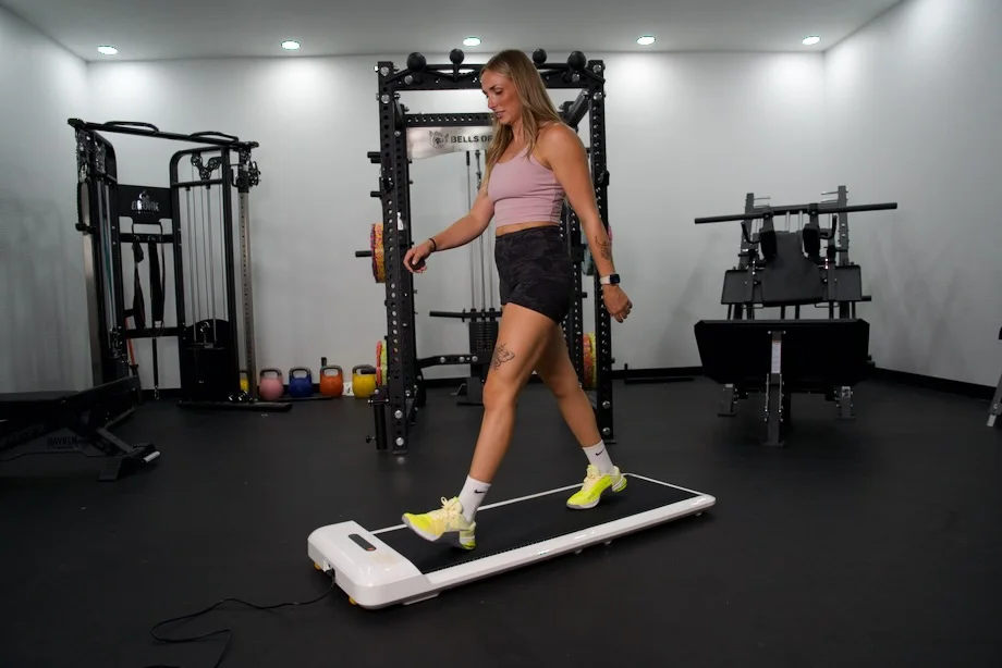 A woman working at a standing desk while walking on a compact under-desk treadmill.
