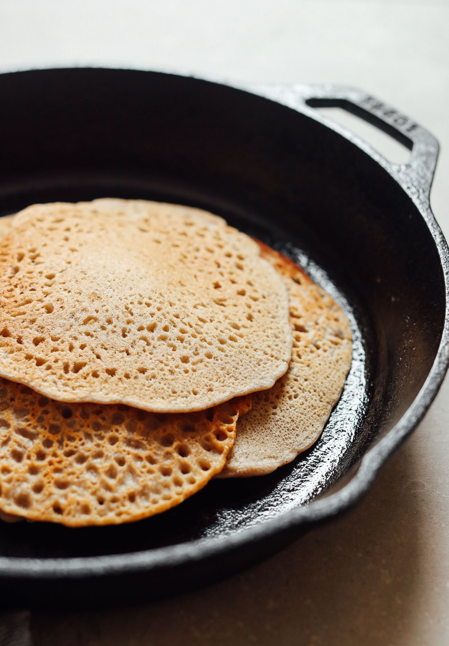 A stack of golden buckwheat crepes being prepared in a cast iron skillet.