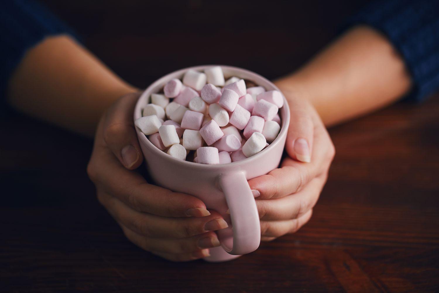 A person holding a warm mug with marshmallows, representing comfort and rest during recovery.