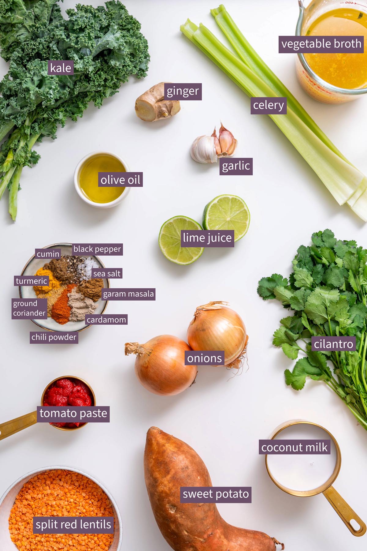 Fresh kale, ginger, garlic, and spices laid out on a white surface.