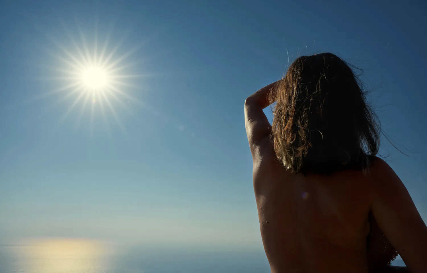 A woman looking out toward the horizon during the day, representing mindfulness of sun exposure.