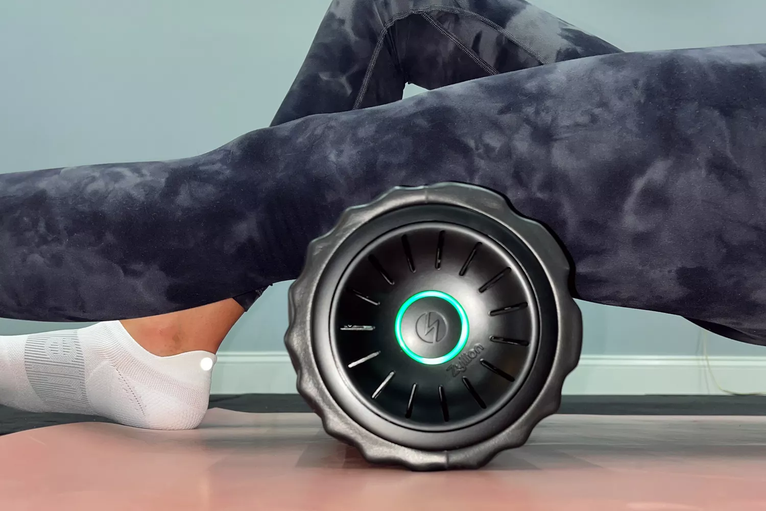 A person using a Zyllion vibrating foam roller on their quadriceps with the power light visible