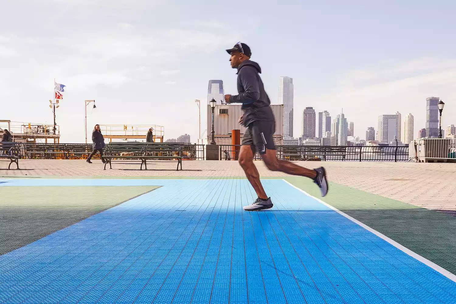 A man running on a blue outdoor track with an urban skyline in the distance.