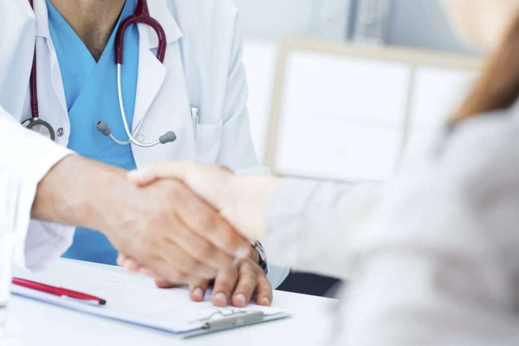 A healthcare professional shaking hands with a patient in a clinical setting.