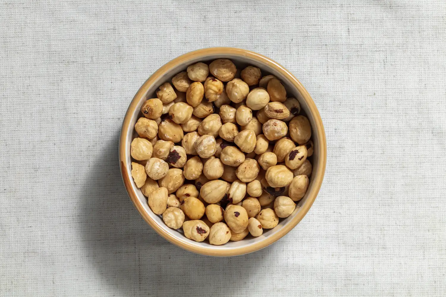 A small wooden bowl filled with whole hazelnuts.