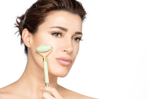 A close-up of a person using a green jade roller on their cheek for lymphatic drainage.