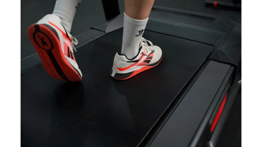 Close-up of a person's feet walking on a treadmill deck, showing the belt texture and side rails.
