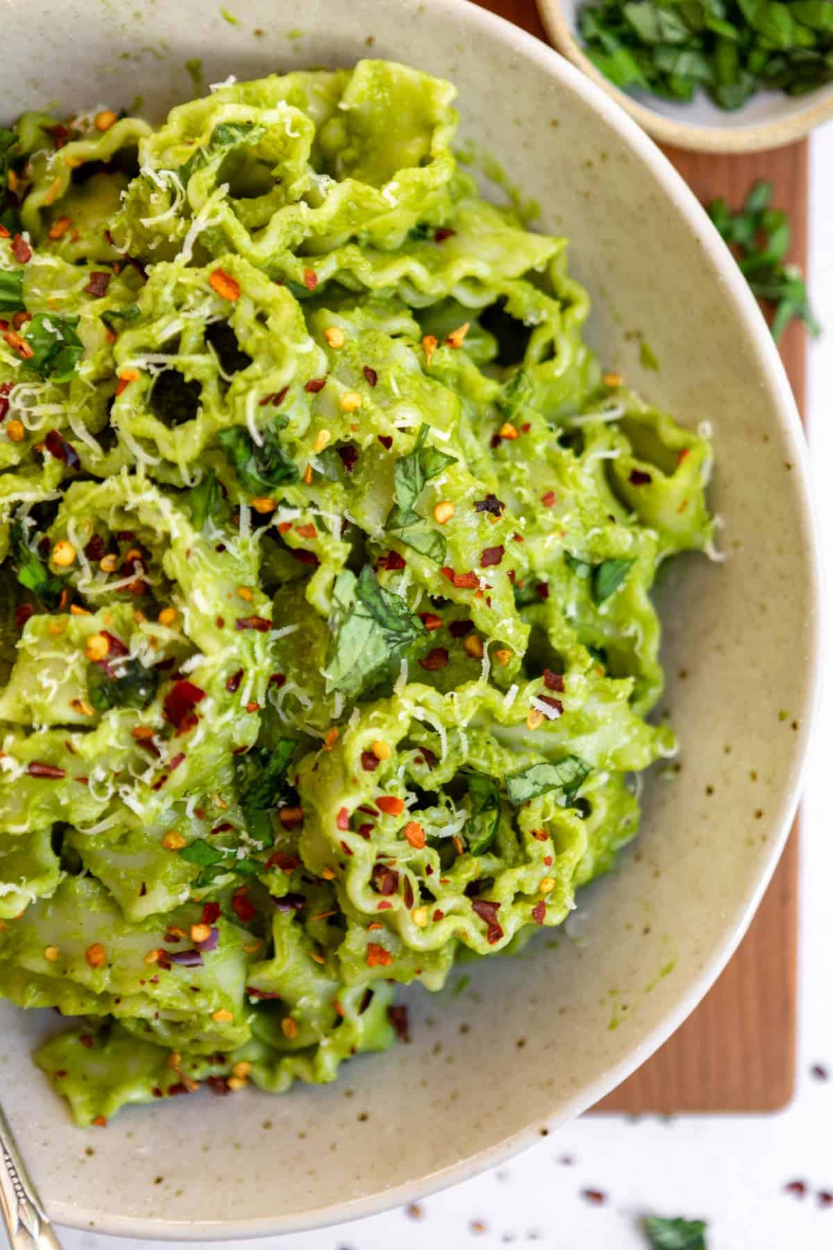 Overhead view of a bowl of mafaldine avocado pesto pasta on a wooden surface.