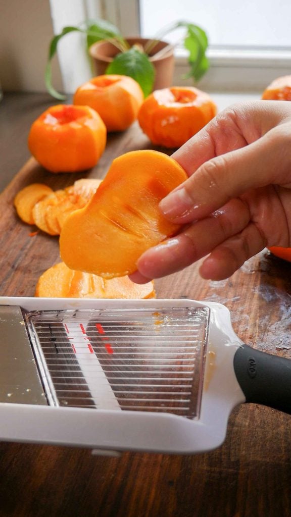 Top-down view of bright orange Fuyu persimmons sliced into uniform 1/8-inch rounds.