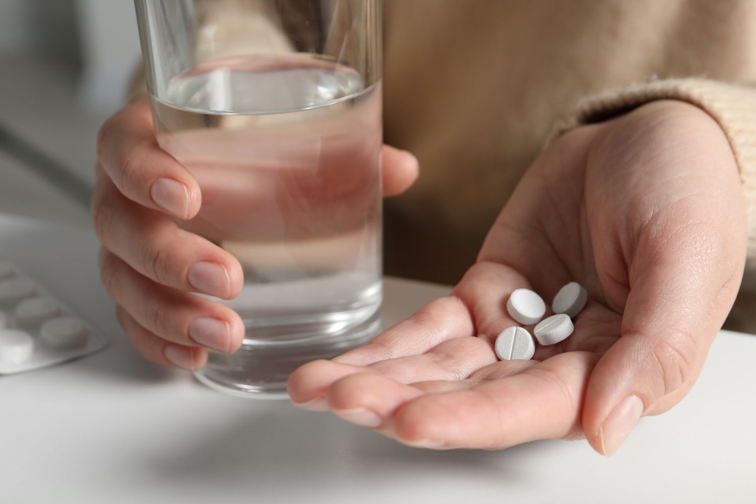 A person holding a glass of water and several white tablets, representing the daily routine of oral GLP-1 medications.